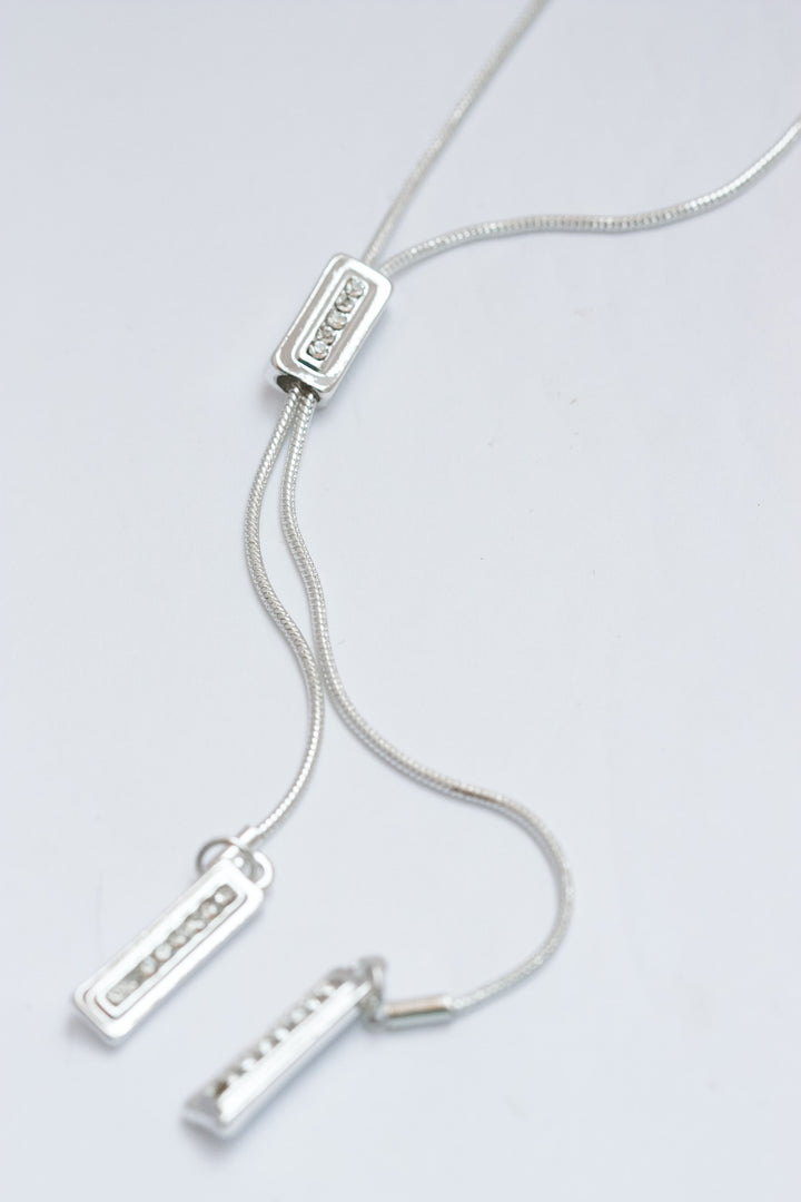 Silver necklace with three pendant charms on a light gray background