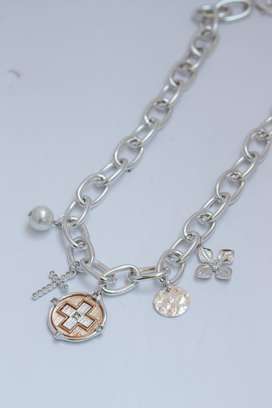 Silver chain necklace with various charms on a light gray background