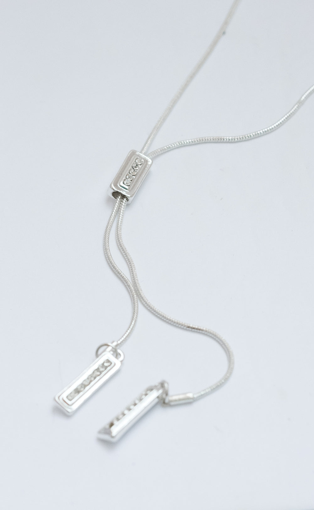 Silver necklace with three pendant bars on a light gray background