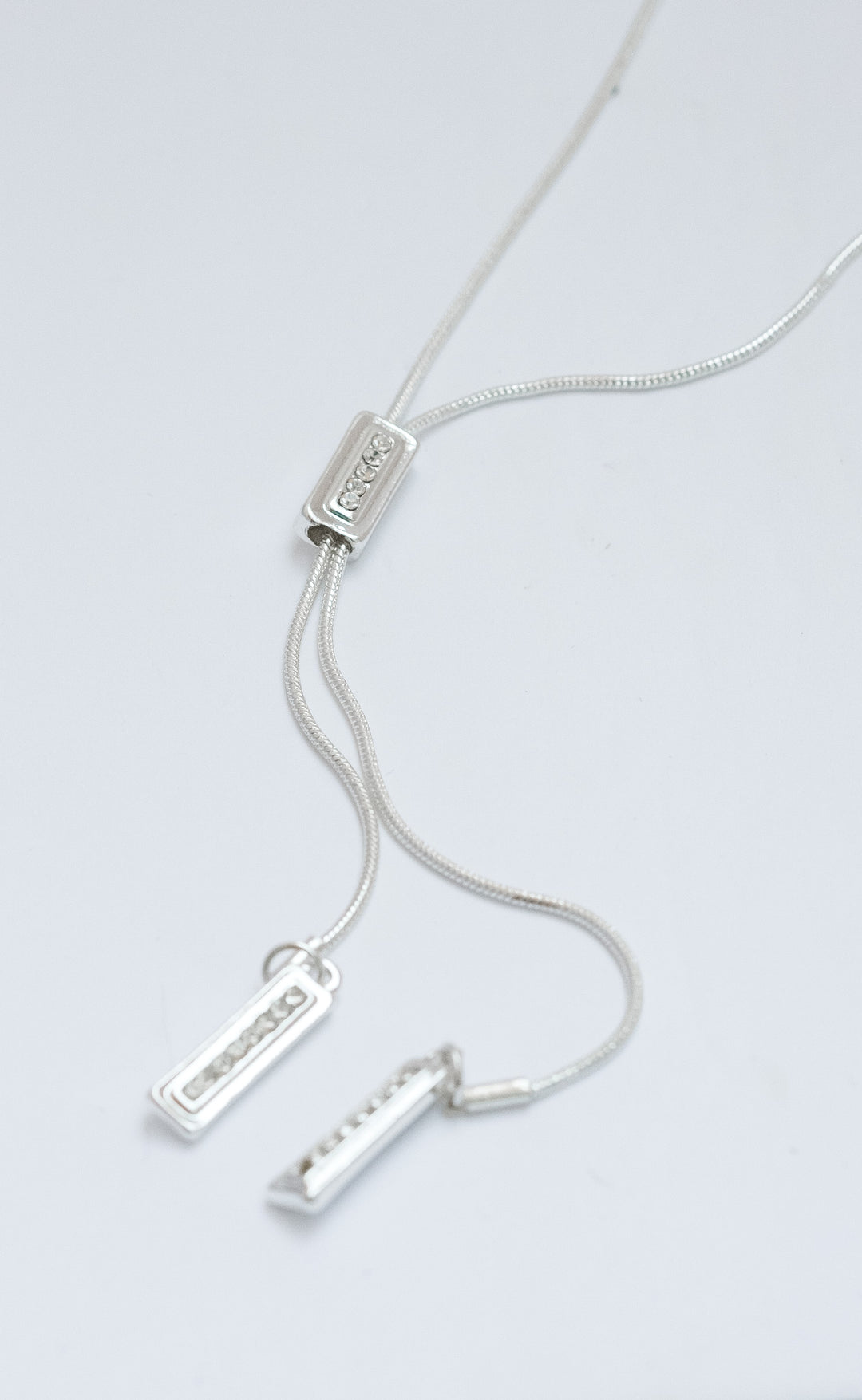 Silver necklace with three pendant bars on a light gray background