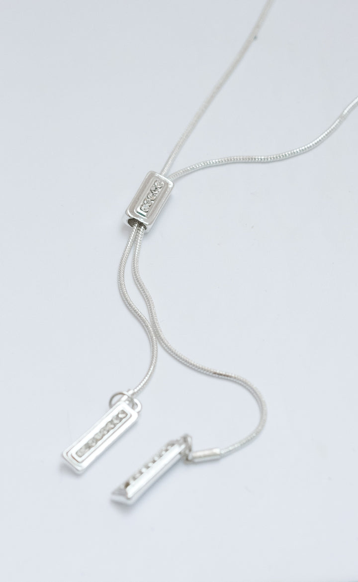 Silver necklace with three pendant bars on a light gray background