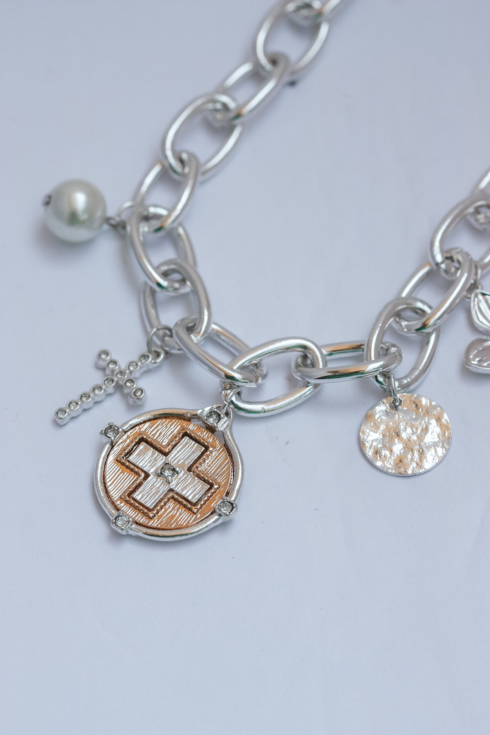 Silver chain necklace with various charms on a light gray background