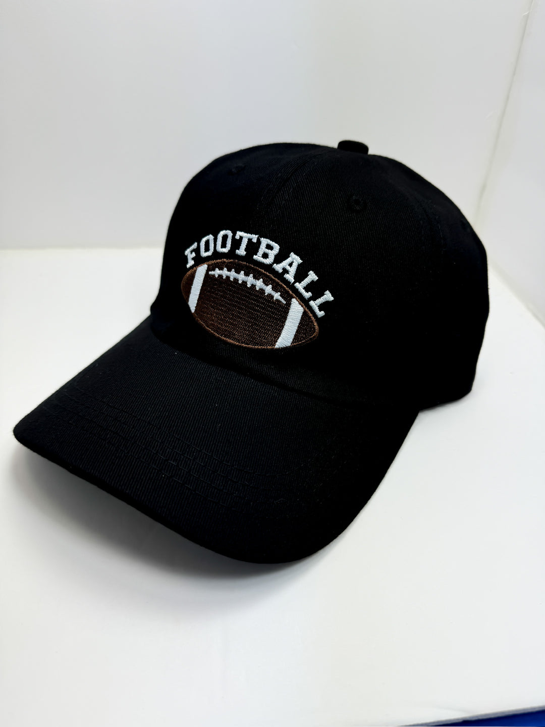 A black baseball cap with an adjustable strap, featuring a brown textured design on the front with the word 'FOOTBALL' and a brown football icon.