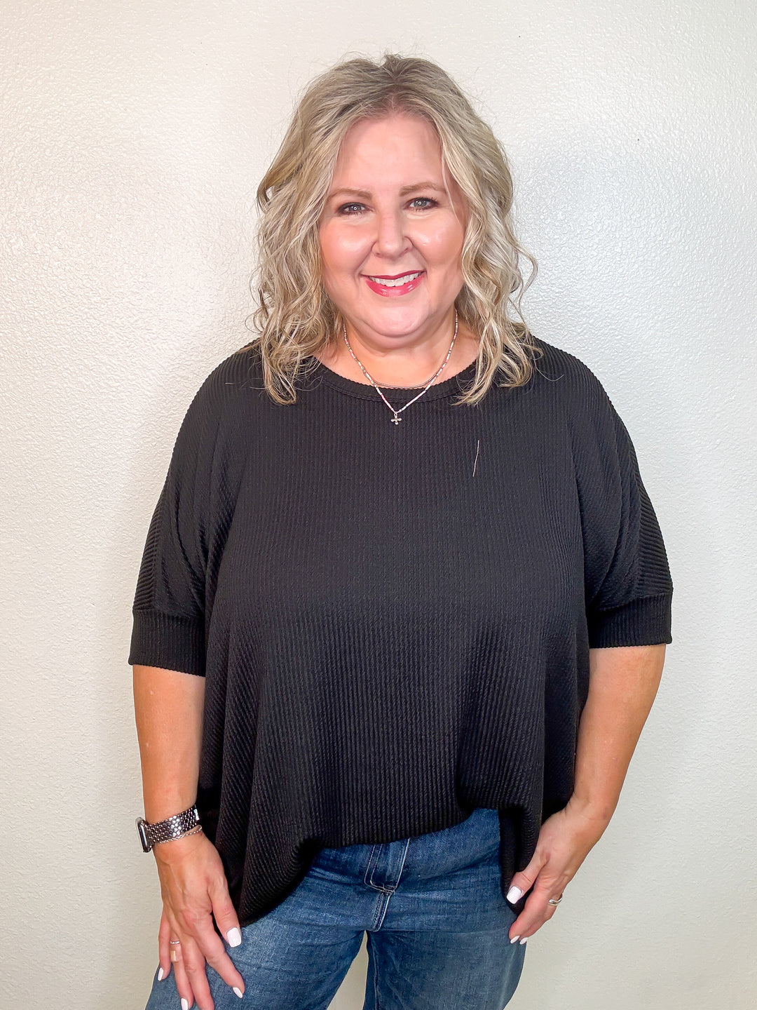 Woman wearing a black top and jeans against a plain background