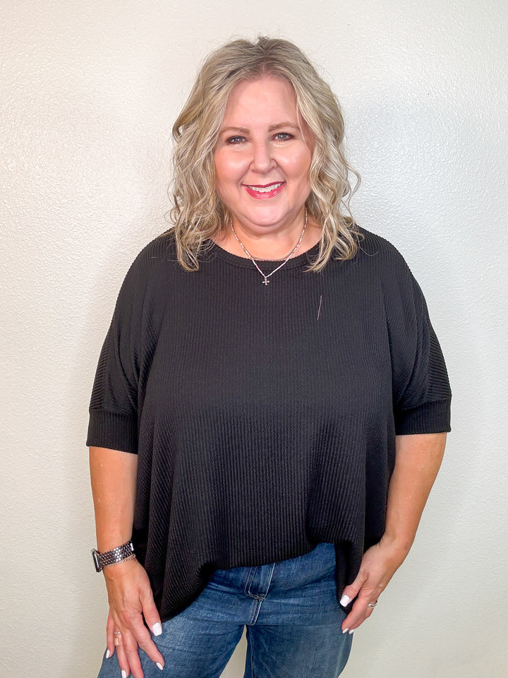 Woman wearing a black top and jeans against a plain background