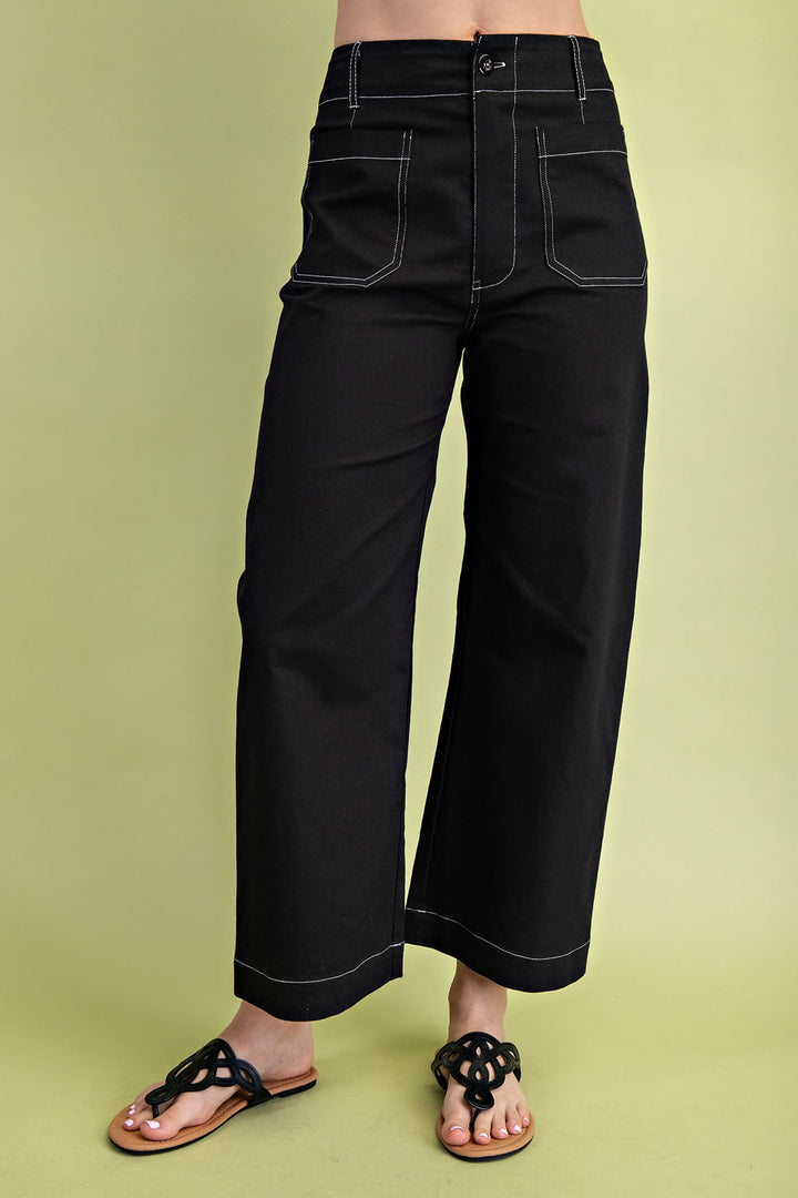 A pair of black cropped wide leg pants with white contrast stitching and rounded front and back pockets, worn with flat sandals.