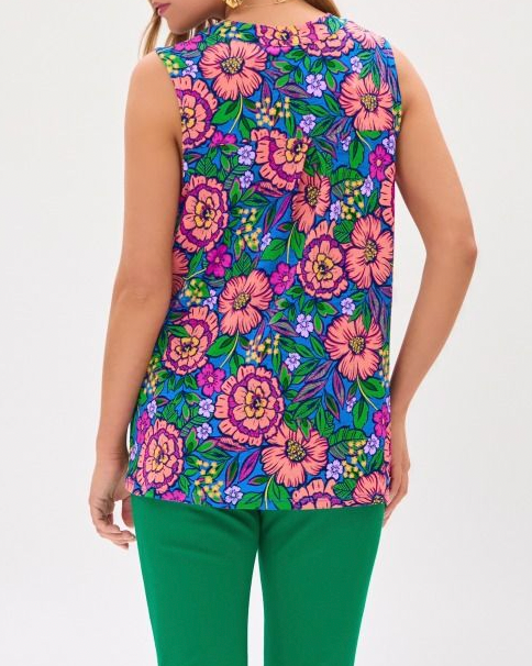 Woman wearing a colorful floral sleeveless top with green pants on a white background