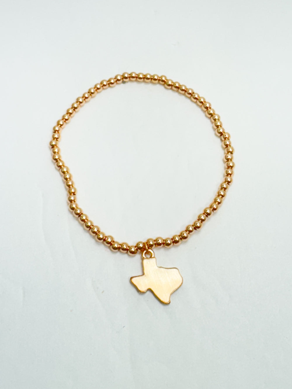 Gold bracelet with a Texas-shaped charm on a light gray background