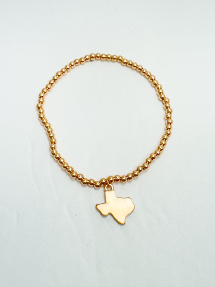 Gold bracelet with a Texas-shaped charm on a light gray background