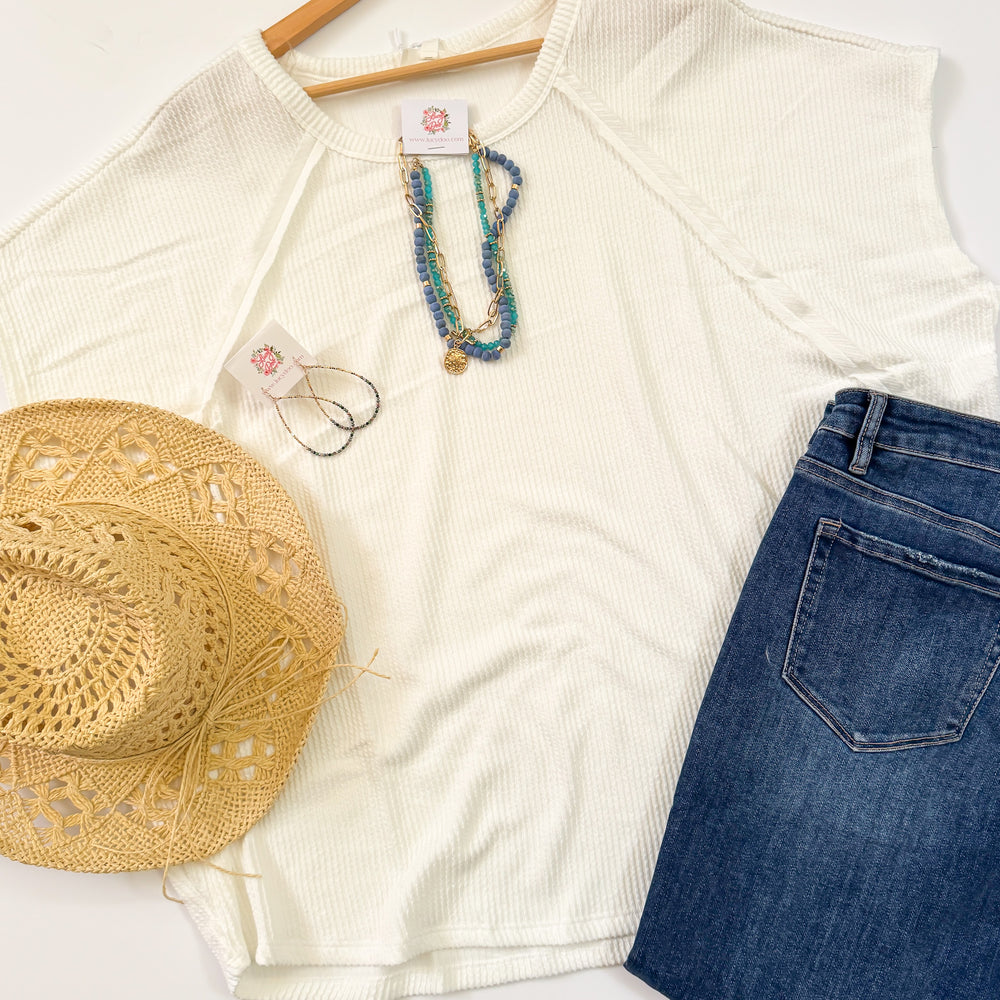 flat lay of cream colored raised rib top with jewelry jeans and hat