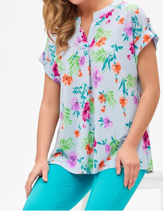 Woman wearing a colorful floral blouse and turquoise pants on a white background