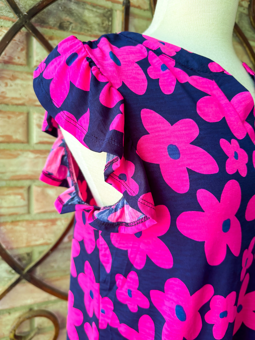 Navy blue dress with pink floral patterns on a mannequin against a brick wall background.