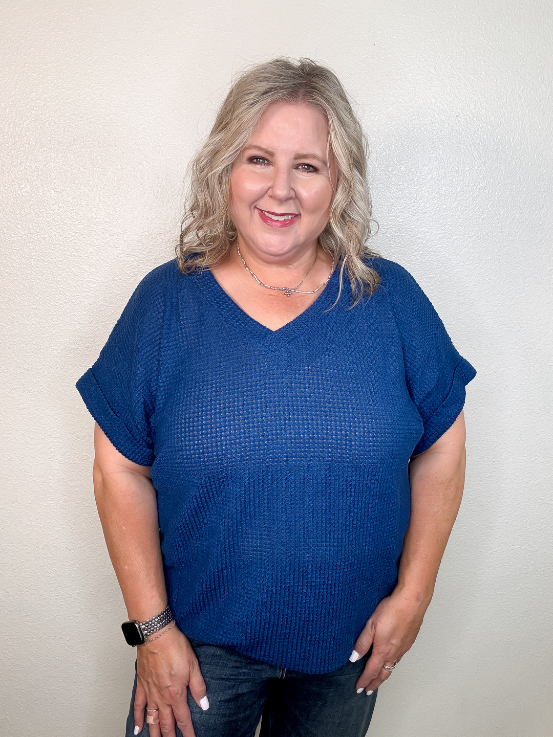 A woman wearing a navy-colored, short-sleeved, v-neck top with a relaxed fit.
