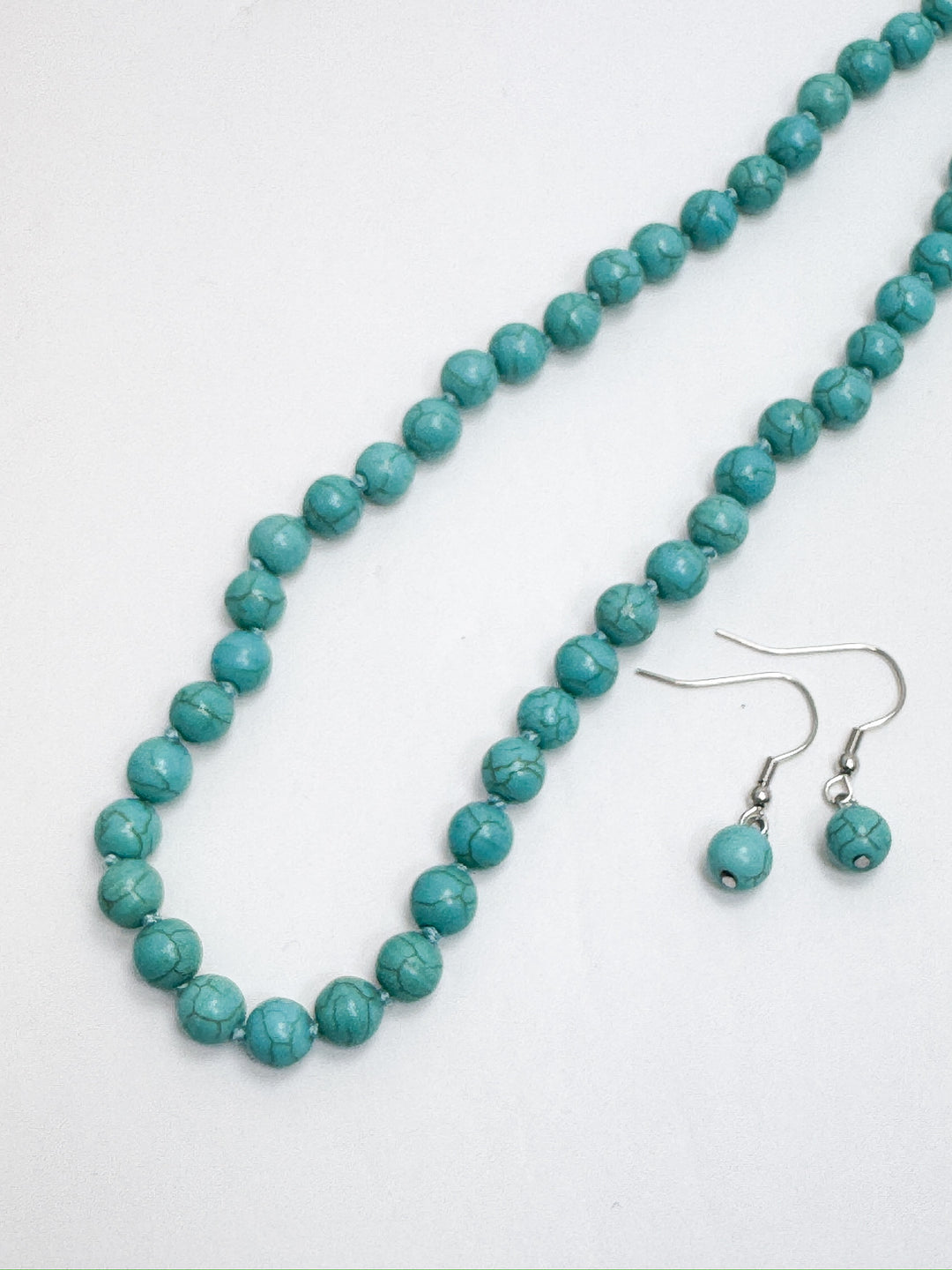 A strand of turquoise bead necklace with matching earrings laid out on a white surface.