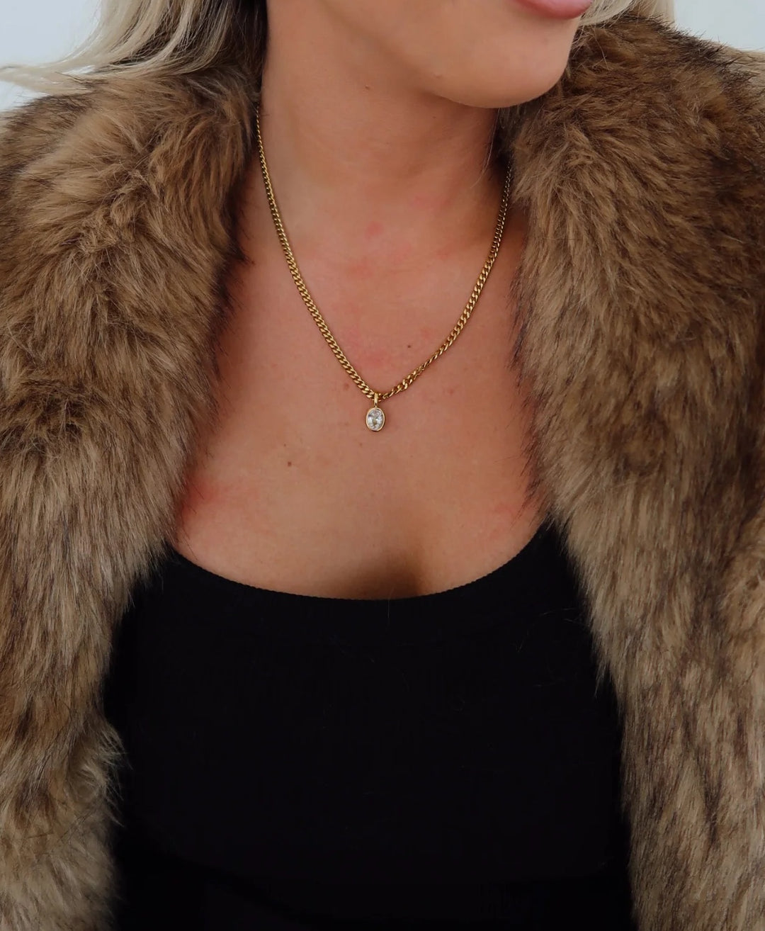 Person wearing a fur coat and gold necklace with a pendant.