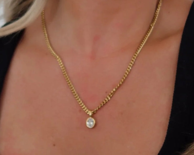 Gold chain necklace with a small round pendant on a person's neck.