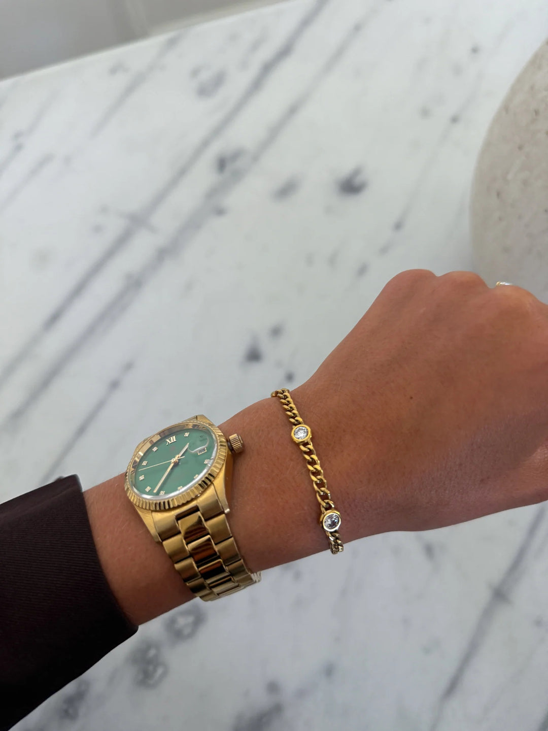 Gold watch and bracelet on a wrist with a marble background