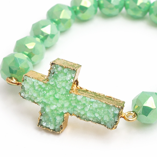 Green beaded bracelet with a gold cross charm on a white background