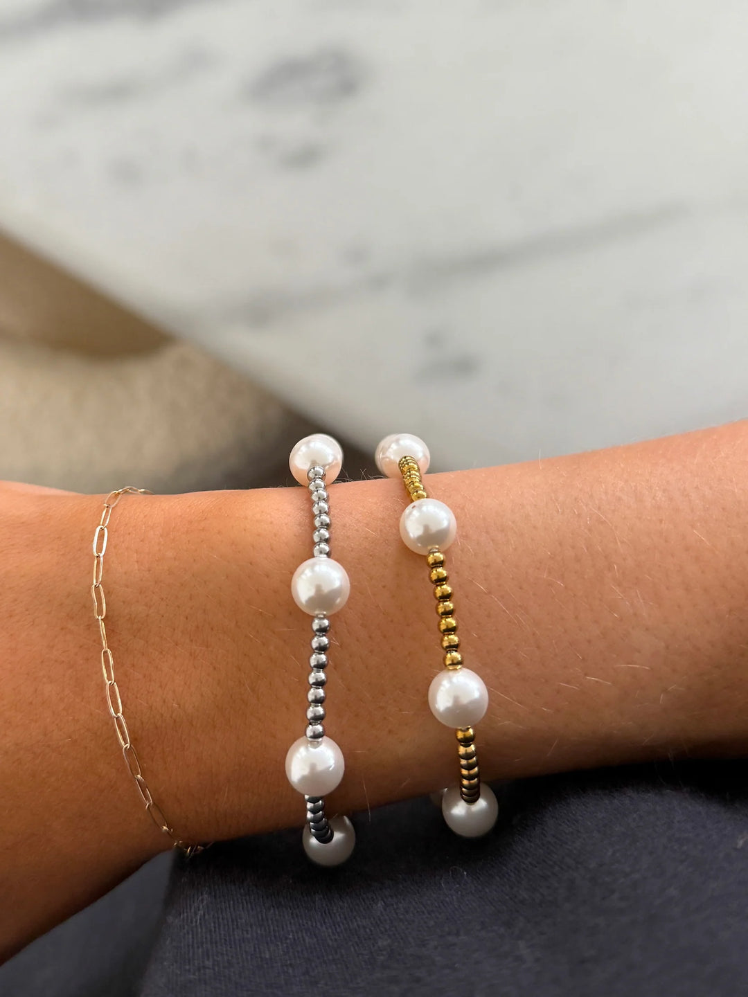 Three pearl bracelets on a wrist with a marble background