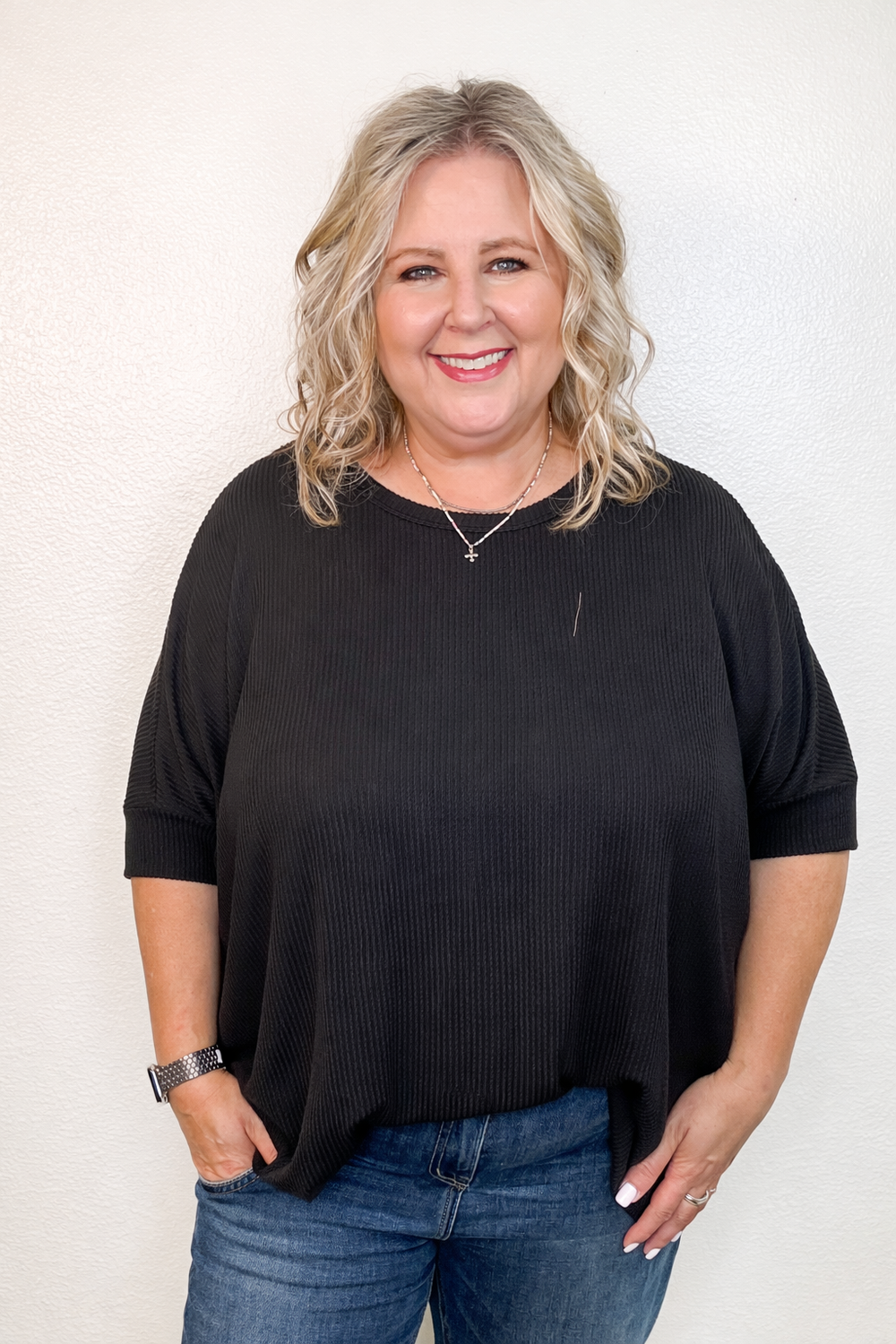 Woman wearing a black top and blue jeans against a white background