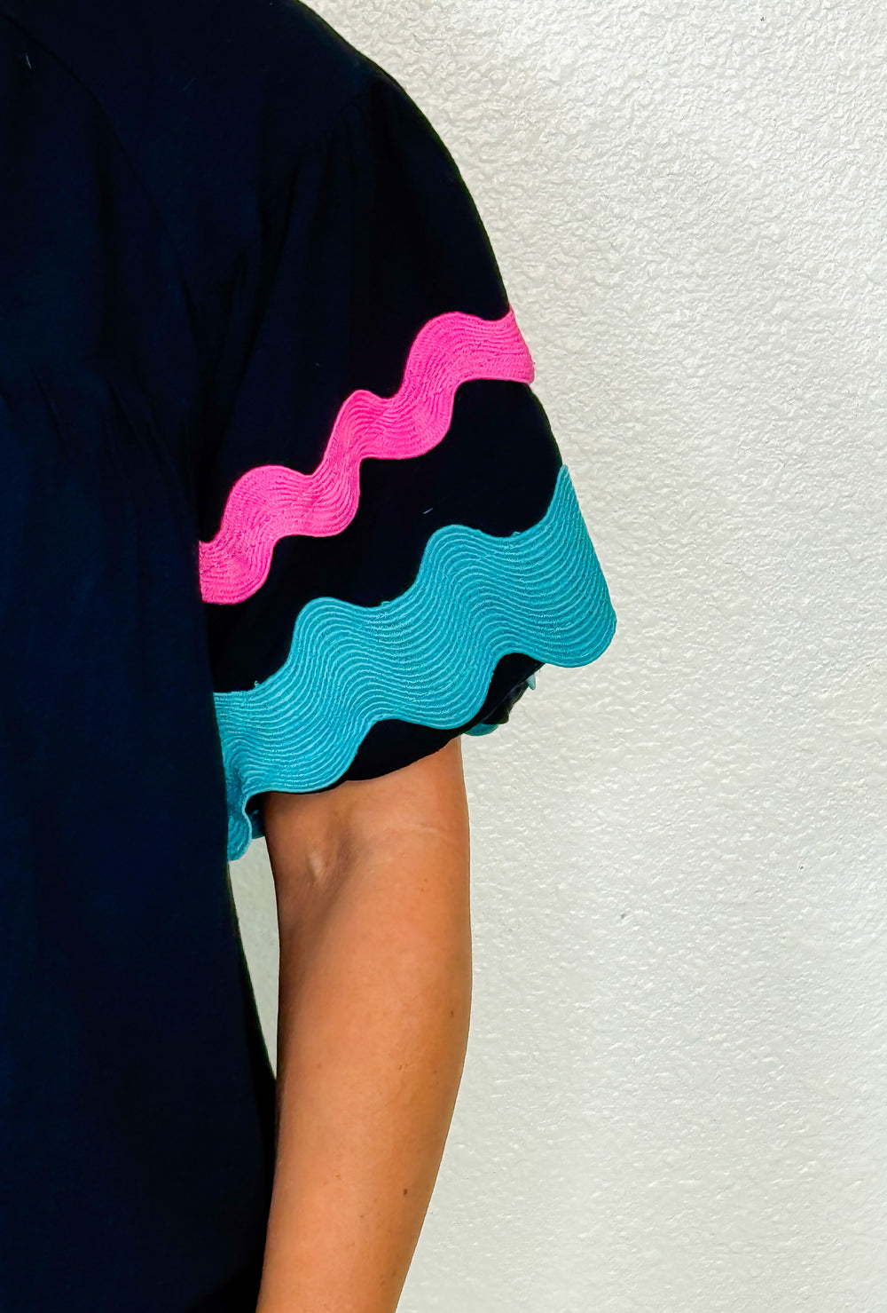 Black dress with pink and blue wavy patterns on a textured white background
