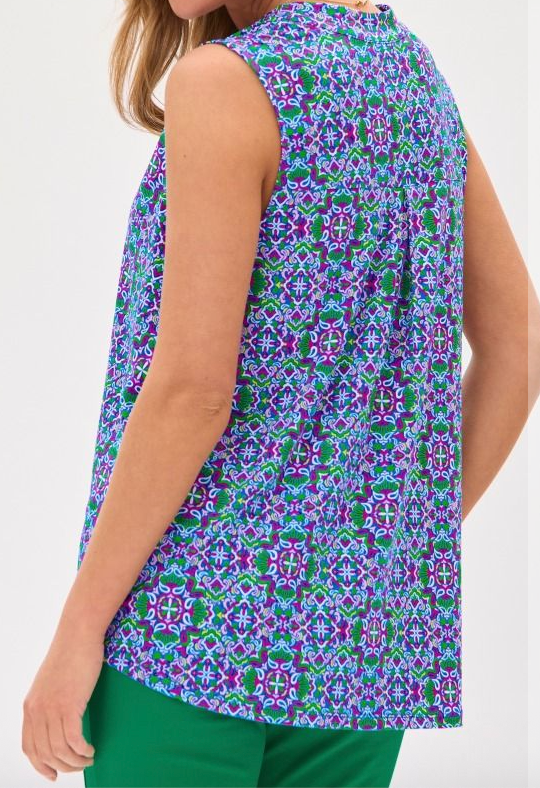 Woman wearing a sleeveless, patterned top with green pants on a white background