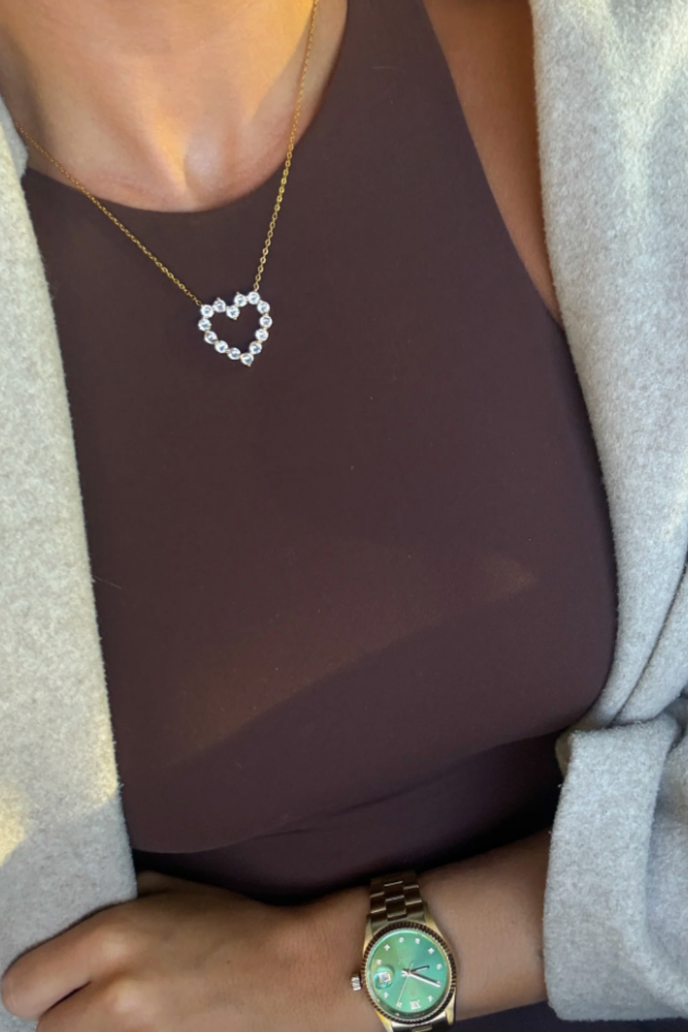 Person wearing a heart-shaped necklace and a watch with a green face.