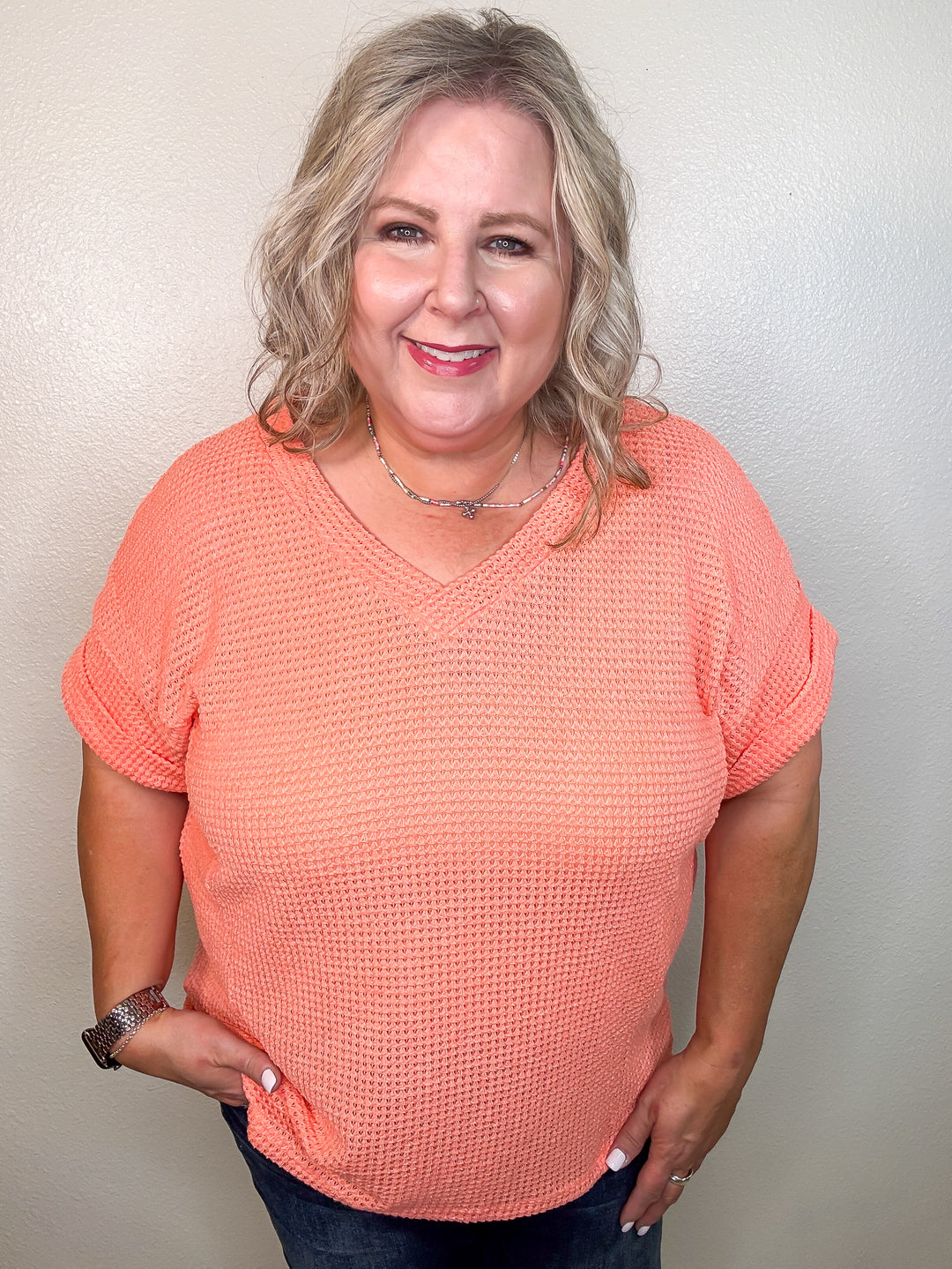 A person wearing a coral-colored, v-neck, short-sleeved top with a waffle knit texture.