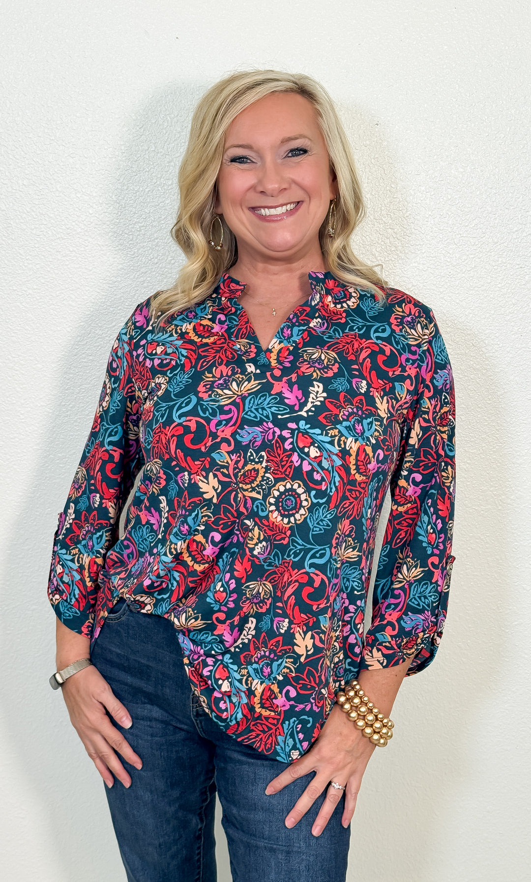 Woman wearing a colorful floral blouse and jeans against a white background