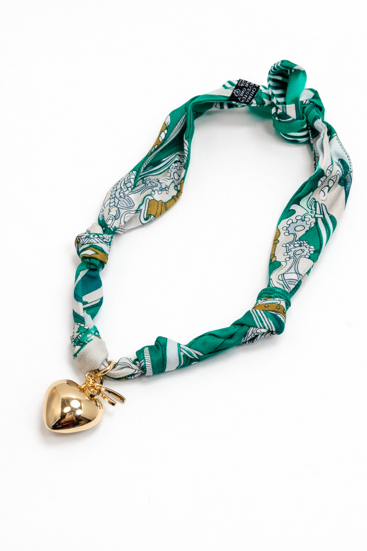 Green patterned dog collar with a gold heart-shaped bell on a white background