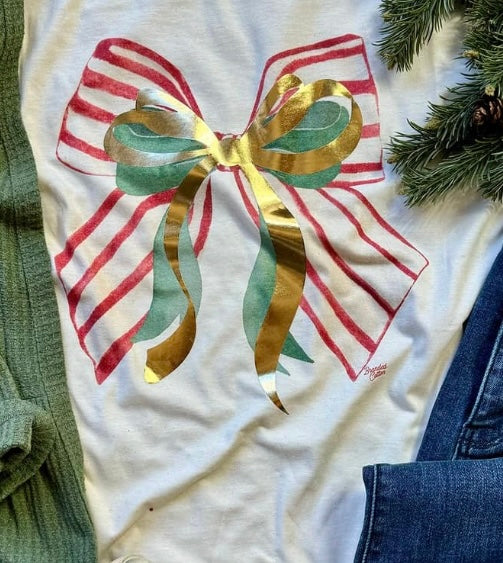 A cream-colored short-sleeve graphic tee with a Christmas-themed design featuring three bows in red and white stripes, green, and metallic gold, tied together.