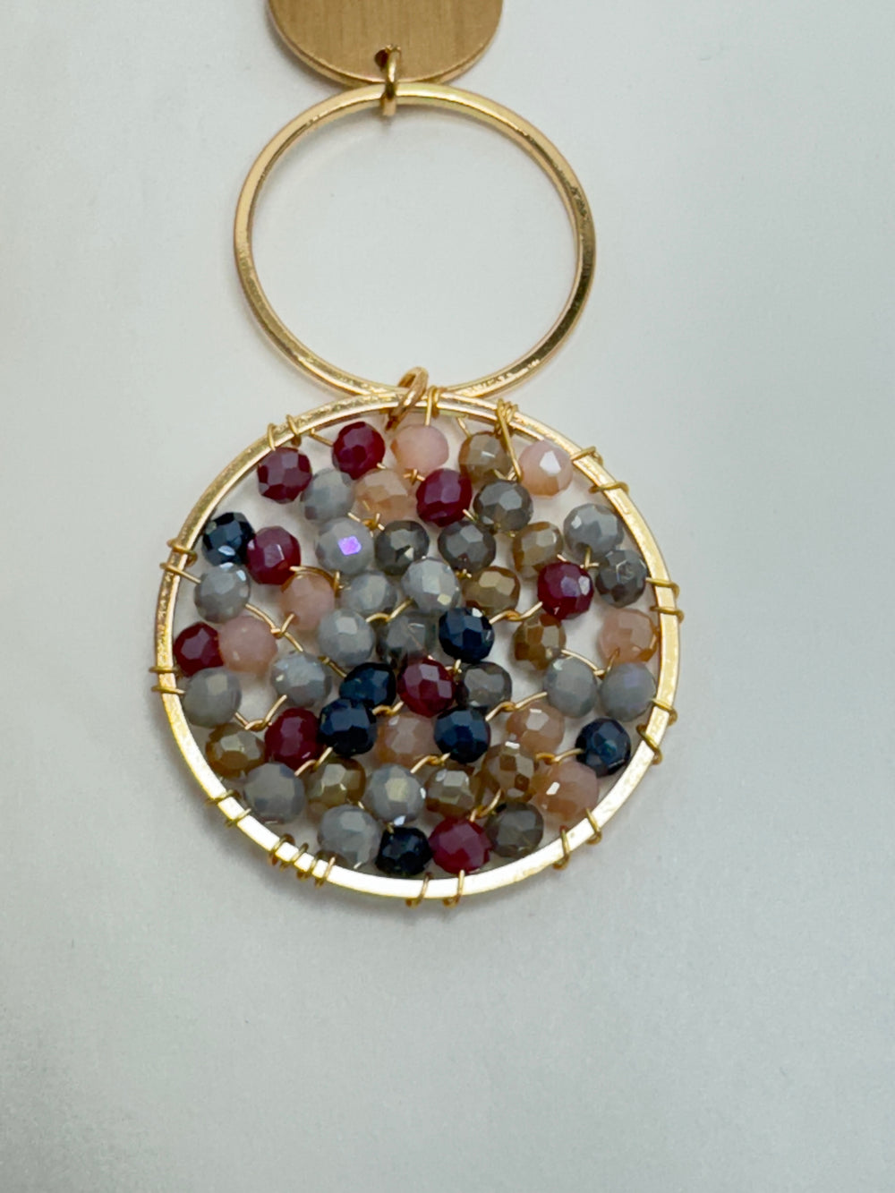 Gold circular pendant with multicolored gemstones on a light gray background