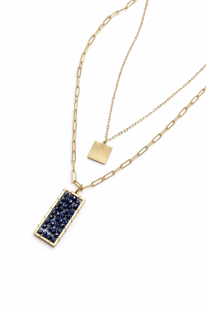 Gold necklace with a blue gemstone pendant on a white background