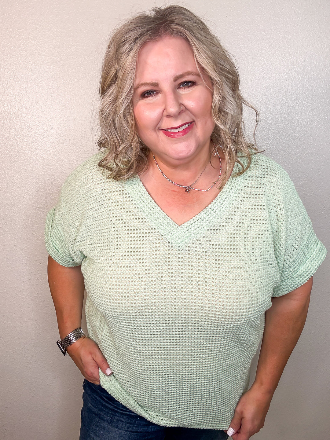 A person wearing a mint green v-neck top with short, cuffed sleeves and angled stitching, paired with jeans.