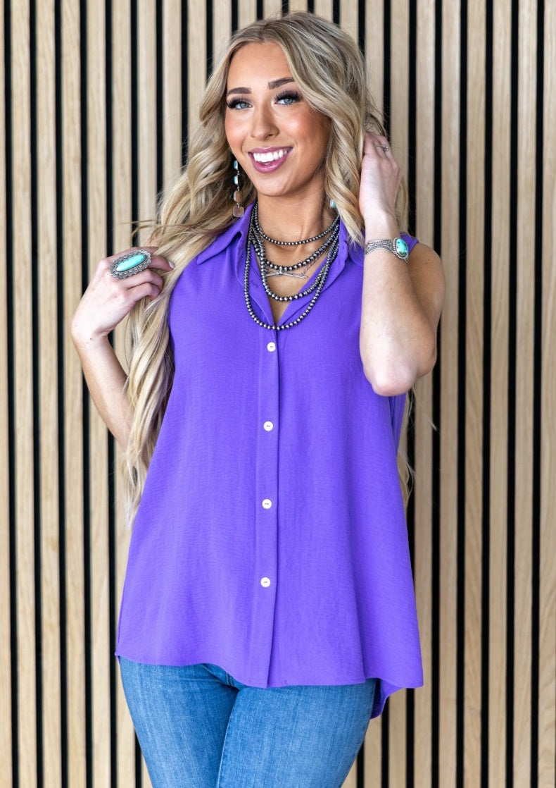Woman wearing a purple sleeveless blouse and blue jeans against a striped background