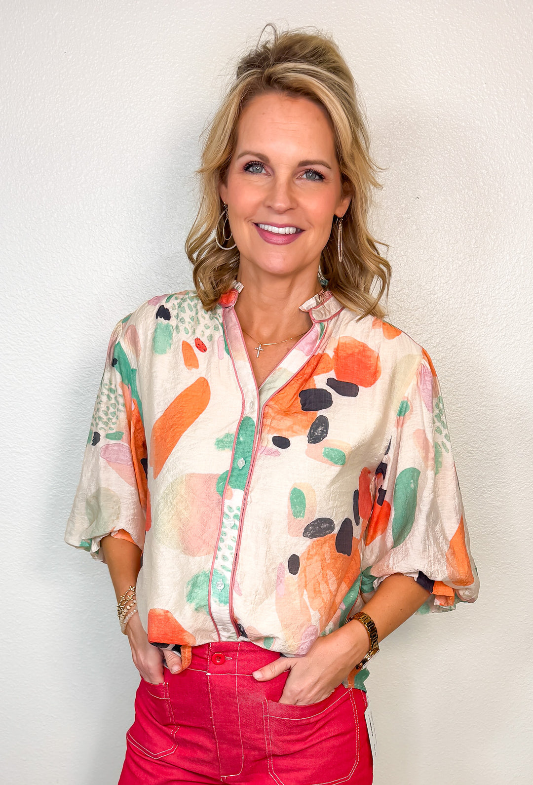 Woman wearing a colorful floral blouse and red pants against a plain background