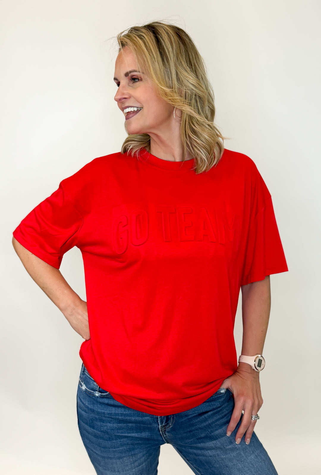 A person wearing a red 'GO TEAM' t-shirt with embossed text on the front, paired with blue jeans.