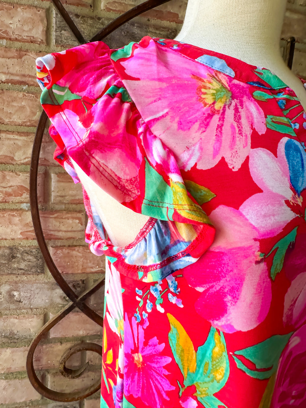 Mannequin wearing a colorful floral dress against a brick wall.