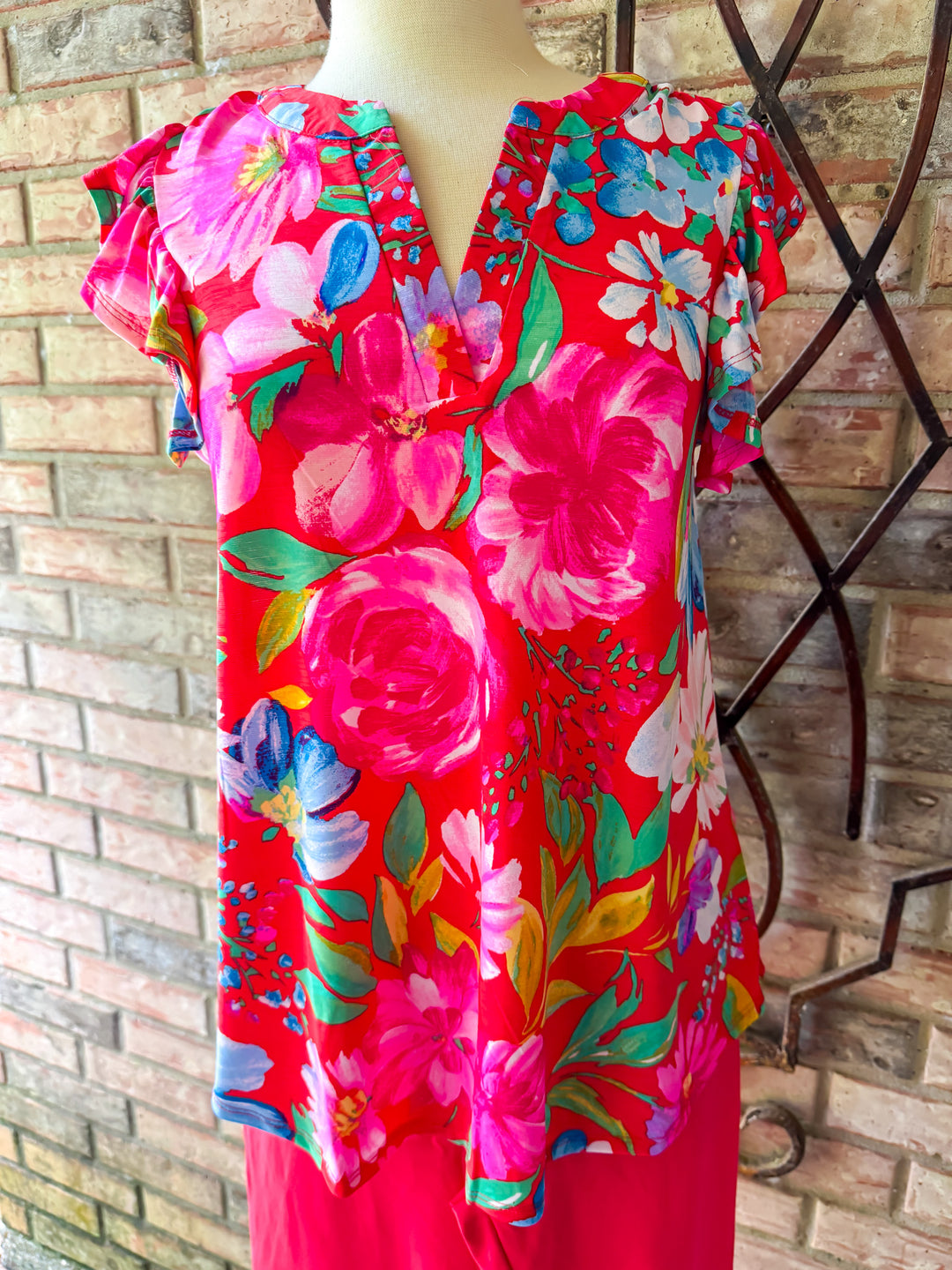 Mannequin wearing a vibrant floral dress against a brick wall.