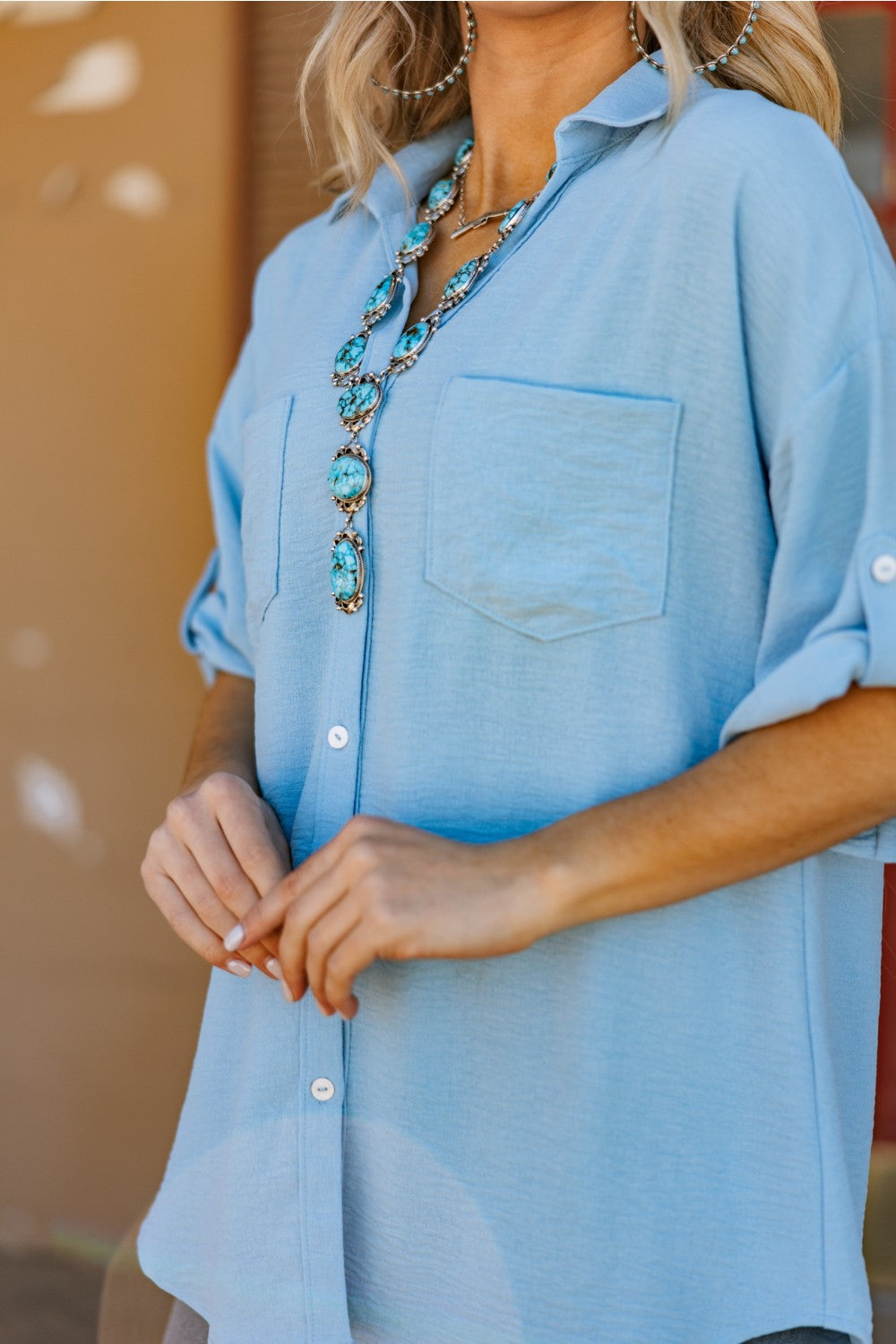 A person wearing a tiffany blue button-down blouse with a classic collar, half sleeves, and front pocket detail. The blouse is made from woven fabric with stretch.