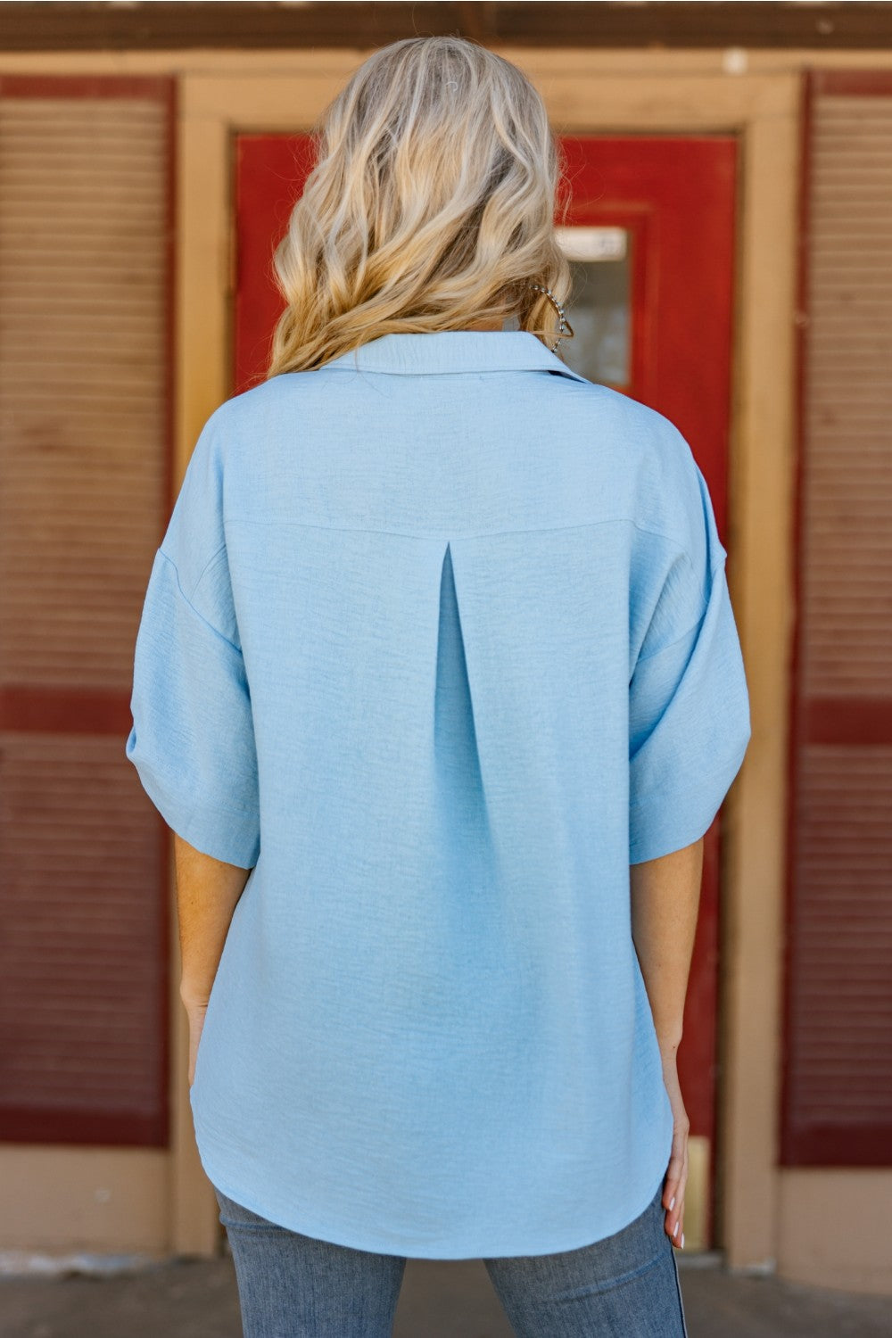 Person wearing a light blue shirt in front of a wooden door.