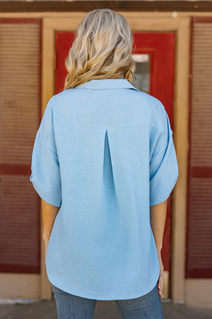 Person wearing a light blue shirt in front of a wooden door.